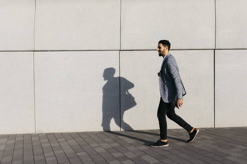 Casual young businessman walking along the wall in the city - JRFF03987