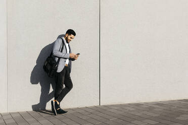 Lässiger junger Geschäftsmann, der ein Mobiltelefon an einer Wand benutzt - JRFF03988