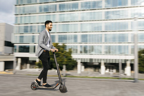 Casual young businessman riding electric scooter in the city - JRFF03994