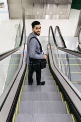 Porträt eines lächelnden jungen Geschäftsmannes auf einer Rolltreppe, der sich umdreht - JRFF03997