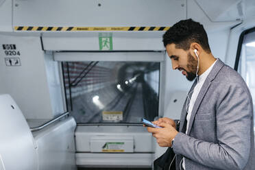 Young businessman with cell phone and earphones on the subway - JRFF04005