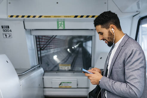 Junger Geschäftsmann mit Mobiltelefon und Kopfhörern in der U-Bahn - JRFF04005