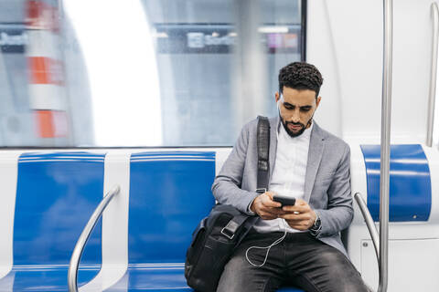 Junger Geschäftsmann mit Mobiltelefon und Kopfhörern in der U-Bahn, lizenzfreies Stockfoto