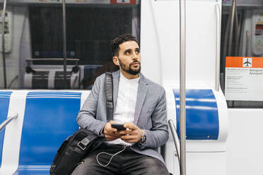 Young businessman with cell phone and earphones on the subway - JRFF04007