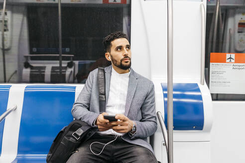Junger Geschäftsmann mit Mobiltelefon und Kopfhörern in der U-Bahn - JRFF04007