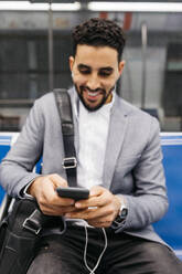 Lächelnder junger Geschäftsmann mit Handy und Kopfhörern in der U-Bahn - JRFF04008