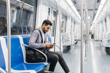 Junger Geschäftsmann mit Mobiltelefon und Kopfhörern in der U-Bahn - JRFF04009