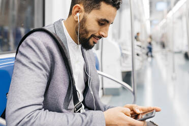 Young businessman with cell phone and earphones on the subway - JRFF04010