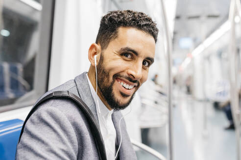 Porträt eines lächelnden jungen Geschäftsmannes mit Kopfhörern in der U-Bahn - JRFF04011