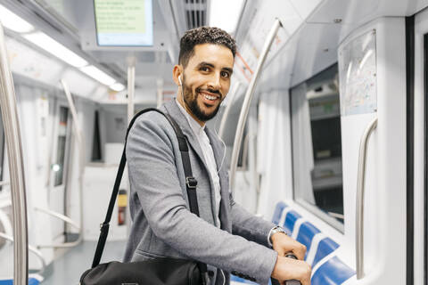 Porträt eines lächelnden jungen Geschäftsmannes mit Kopfhörern in der U-Bahn, lizenzfreies Stockfoto