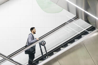 Lächelnder junger Geschäftsmann mit Elektroroller auf Rolltreppe - JRFF04019