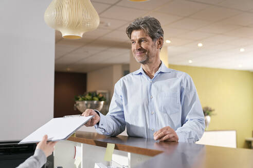 Patient handing over registration form at reception in a medical practice - PHDF00041