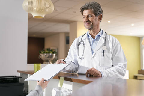 Arzt bei der Aufnahme der Krankenakte am Empfang in seiner Arztpraxis, lizenzfreies Stockfoto