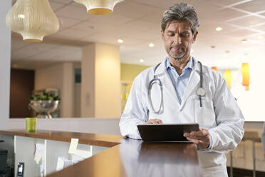 Arzt benutzt Tablet an der Rezeption in seiner Arztpraxis - PHDF00044