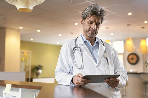 Arzt benutzt Tablet an der Rezeption in seiner Arztpraxis, lizenzfreies Stockfoto