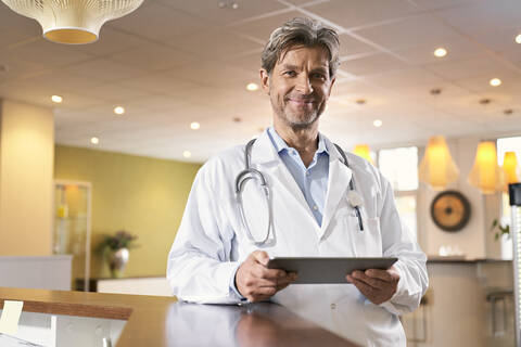 Portrait of confident doctor with tablet at reception in his medical practice stock photo