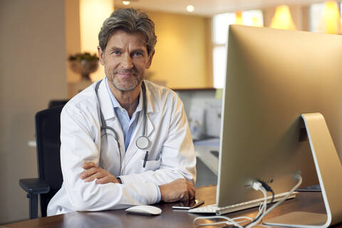 Porträt eines selbstbewussten Arztes am Schreibtisch in seiner Arztpraxis, lizenzfreies Stockfoto
