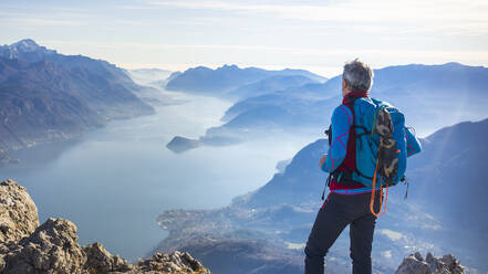 Hiker standing on mountain, looking at Lake Como, Italy - MCVF00193