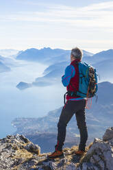 Hiker standing on mountain, looking at Lake Como, Italy - MCVF00194