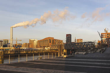 Deutschland, Hamburg, HafenCity in der Morgendämmerung mit Rauch aus Industrieschornsteinen im Hintergrund - ASCF01069