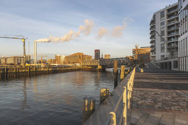 Deutschland, Hamburg, HafenCity in der Morgendämmerung mit Rauch aus Industrieschornsteinen im Hintergrund - ASCF01071