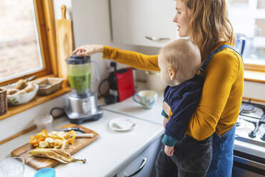 Frau in der Küche bereitet gesunden Smoothie zu und hält ihren kleinen Sohn - WPEF02455