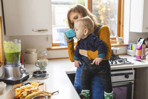 Frau in der Küche bereitet gesunden Smoothie zu und hält ihren kleinen Sohn - WPEF02456