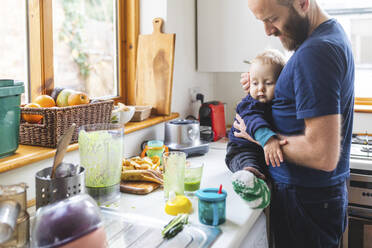 Mann in der Küche, der Essen zubereitet und mit seinem Sohn kuschelt - WPEF02460