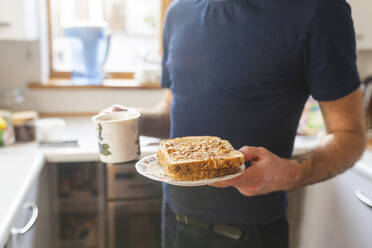 Nahaufnahme eines Mannes in der Küche, der einen Teller mit Sandwich und einen Becher hält - WPEF02469