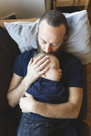 Vater küsst seinen schlafenden Sohn auf dem Sofa, lizenzfreies Stockfoto