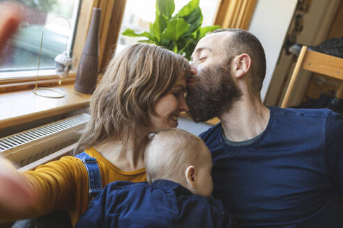 Selfie einer liebevollen Familie auf dem Sofa mit schlafendem kleinen Sohn - WPEF02494