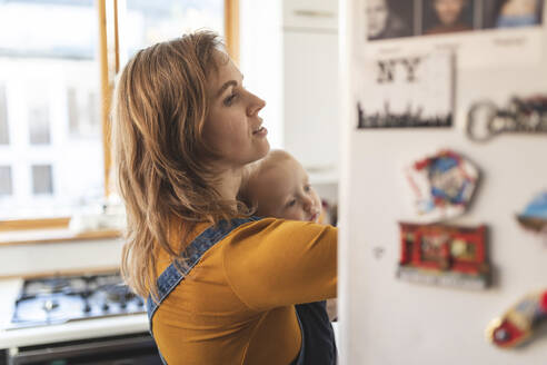 Frau in der Küche öffnet den Kühlschrank und hält ihren Sohn - WPEF02500