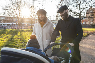 Happy couple with little son in a pushchair at park - WPEF02502