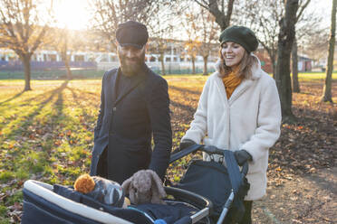 Happy couple with little son in a pushchair at park - WPEF02505