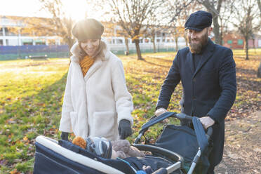 Glückliches Paar mit kleinem Sohn im Kinderwagen im Park - WPEF02506