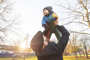 Man lifting up his happy baby son at park - WPEF02510