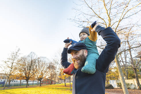 Glücklicher Mann trägt seinen kleinen Sohn im Park auf den Schultern - WPEF02511