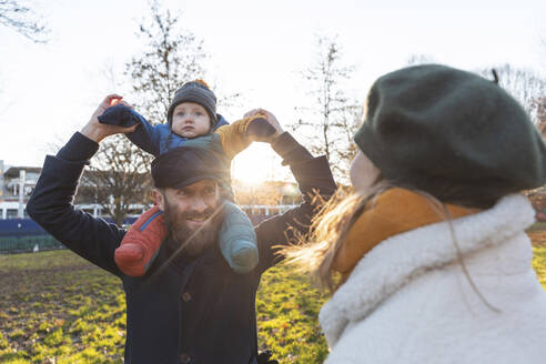 Glücklicher Mann mit Frau, die seinen kleinen Sohn im Park auf den Schultern trägt - WPEF02512