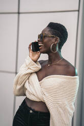 Porträt einer lachenden jungen Frau mit Sonnenbrille am Telefon - MPPF00445