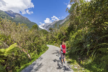 New Zealand, Westland District, Franz Josef, Female backpacker taking break on scenic road leading to Franz Josef Glacier - FOF11446