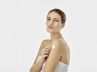 Portrait of woman pouting mouth applying body cream on her arm - RORF01985