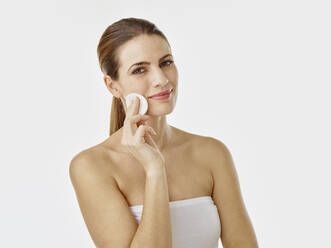 Portrait of smiling woman cleaning face with cotton pad - RORF01998