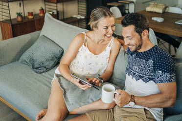 Happy relaxed couple sitting on couch in living room sharing a tablet - MPPF00462