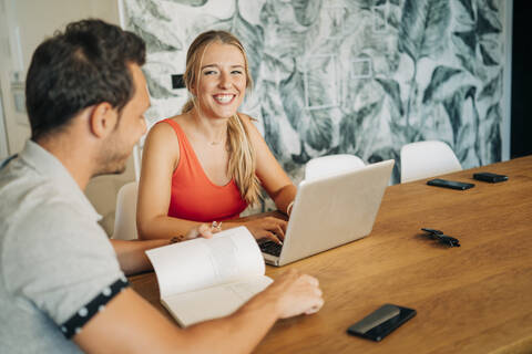 Glückliches Paar sitzt am Tisch mit Laptop und Buch, lizenzfreies Stockfoto