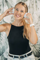 Porträt einer lächelnden Frau, die mit Kopfhörern Musik hört - MPPF00478