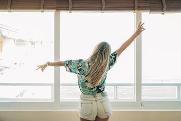 Rückansicht einer Frau mit Hawaii-Hemd am Fenster - MPPF00483