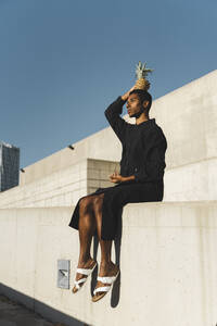 Junger Mann in schwarzem Kaftan balanciert eine Ananas auf seinem Kopf - AFVF05124