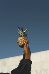 Close-up of man holding a pineapple under blue sky - AFVF05130