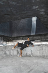 Junger Mann in schwarzem Kaftan auf einer Betonmauer liegend im Freien - AFVF05142
