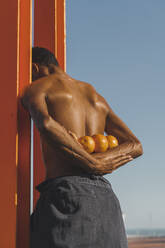 Barechested young man holding oranges outdoors - AFVF05166